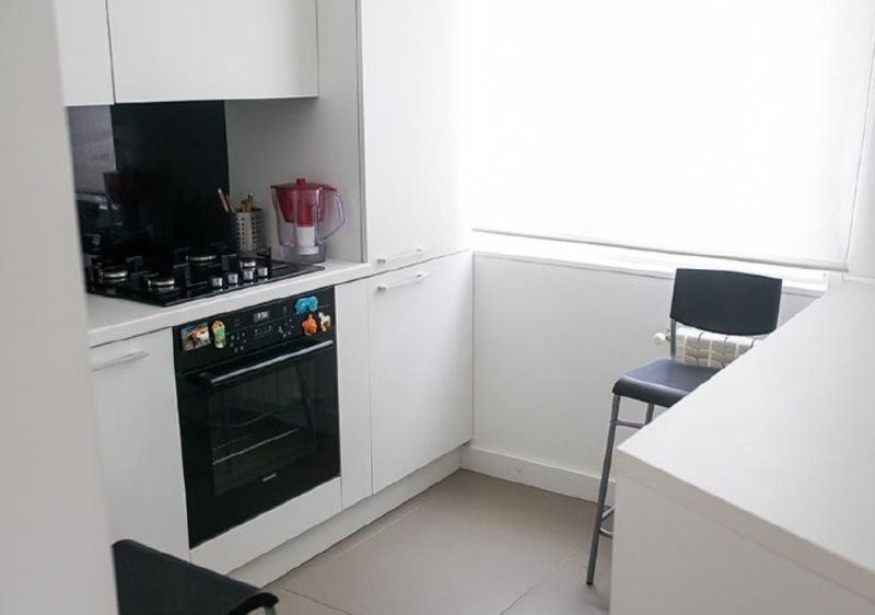 Μαύρες συσκευές σε μια μικρή κουζίνα με λευκά έπιπλα