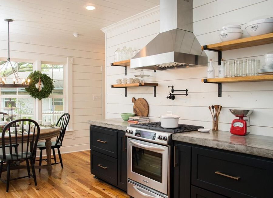 Μεταλλική κουκούλα σε τοίχο κουζίνας ανάμεσα σε ξύλινα ράφια